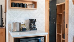 Una kitchenette compacta con microondas, cafetera y estantes para guardar objetos.