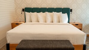 Una cama bien hecha con un cabecero verde, ropa de cama blanca y un banco al pie.