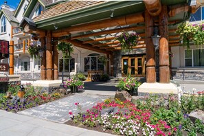 A building with a wooden facade, a stone entrance, and a flower garden in front. - Cozy Room in Banff with Air-Conditioning (Banff)