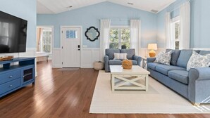 A living room with a blue sofa, a white coffee table, and a television on a blue stand. - Sea La Vie𓇼Central Location𓇼Cozy𓇼Fire Pit (Oak Island)