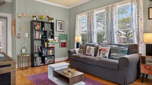 A living room with a grey sofa, a bookshelf, a coffee table, and a window with curtains. - New! Stunning Pet-Friendly Home + 3 Min to DT! (Seguin)