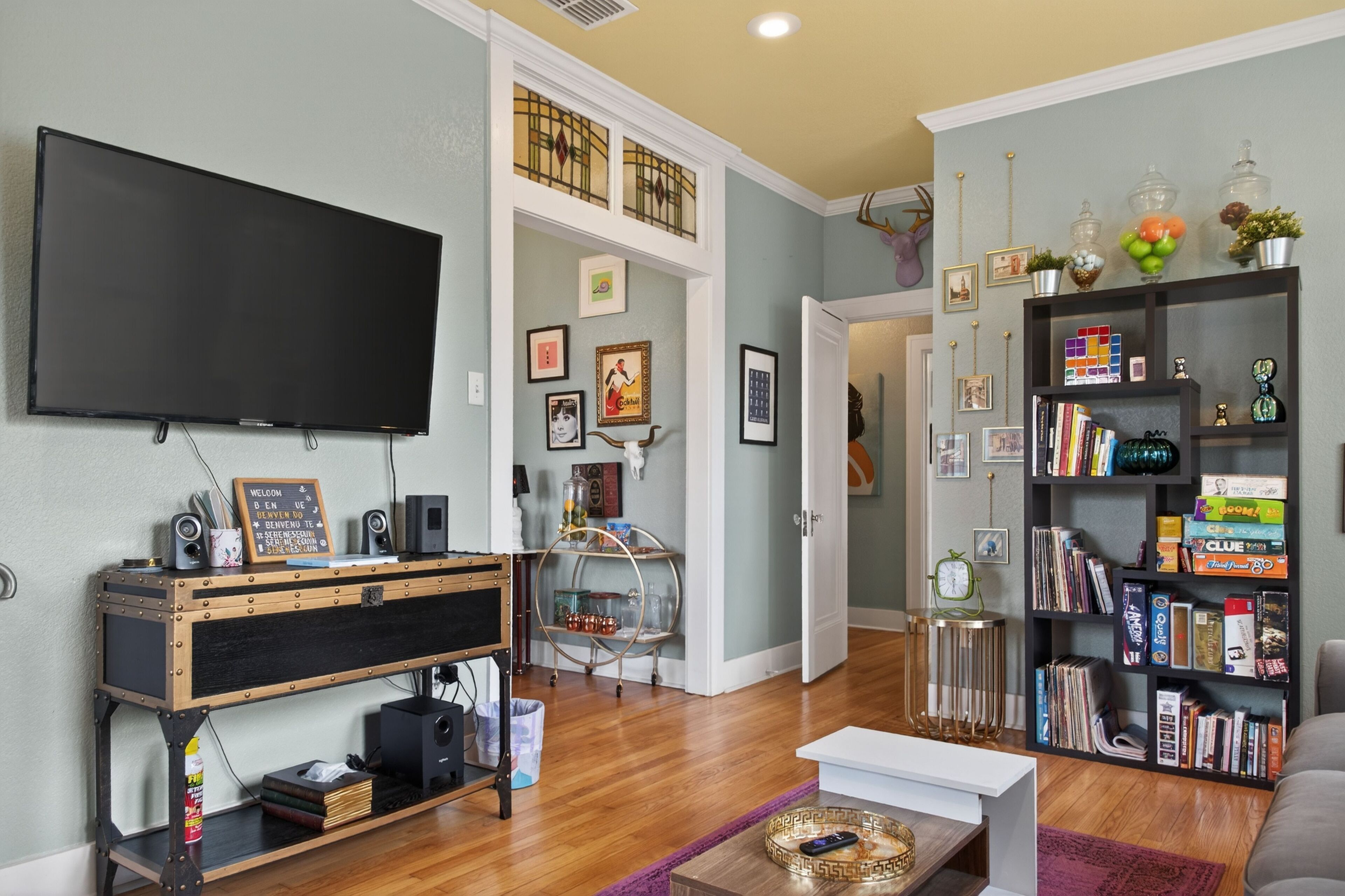 A living room with a flat-screen TV, a wooden entertainment unit, a bookshelf, and a door leading to another room.