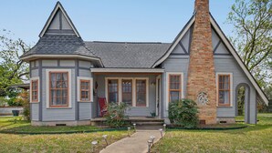 A two-story house with a prominent brick chimney, a covered front porch, and a small garden. - New! Stunning Pet-Friendly Home + 3 Min to DT! (Seguin)