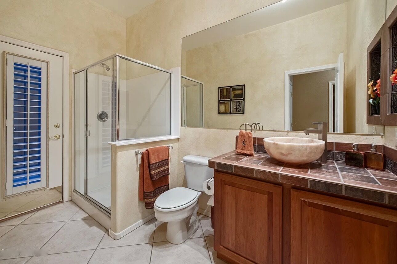 A bathroom with a glass shower enclosure, a white toilet, a large mirror, and a wooden vanity with a marble sink.