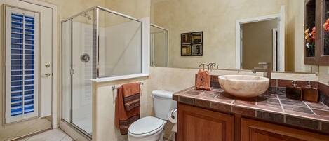 A bathroom with a glass shower enclosure, a white toilet, a large mirror, and a wooden vanity with a marble sink.