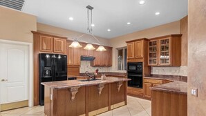 A kitchen with wooden cabinets, a black refrigerator, a large island with a sink, and pendant lighting. - Beautiful Gold Canyon home, Mt Views, Pool, Private setting (Gold Canyon)