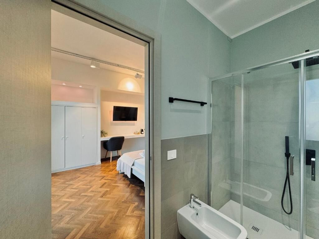 A modern bathroom with a glass shower enclosure, a white sink, and a wooden floor.