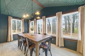 Ein Esszimmer mit einem Holztisch, sechs Stühlen, einer Blumenvase und großen Fenstern mit Vorhängen.