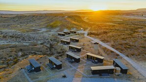 An aerial view of a remote, modern accommodation with multiple cabins, arranged in a linear formation along a dirt road, set in a desert landscape. - Stellar Retreat at Big Bend - Cabin #1 (Terlingua)