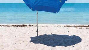 A blue beach umbrella with a logo on the side, standing on a sandy beach with clear blue water in the background. - 3bdrm 3bath Luxury Condo Across from Kamaole Beach Kihei Maui Full AC Sleeps 8 (Kihei)