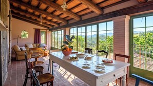 A dining area with a table set for four, a sofa, and a view of vineyards through large windows.