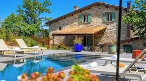 Ein Steinhaus mit Schwimmbad, Sitzgelegenheiten im Freien und einer überdachten Terrasse.