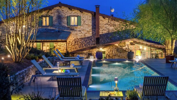 A stone house with a swimming pool, outdoor seating, and a well-lit patio area.