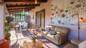 A cozy living room with a leather sofa, a dining table with chairs, a large window, and a floral wall mural.