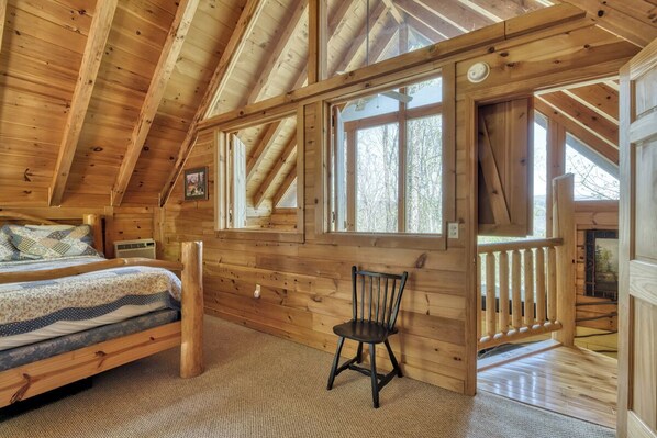 A wooden cabin room with a bed, a chair, and large windows. - Dancing Dragonfly (Sevierville)