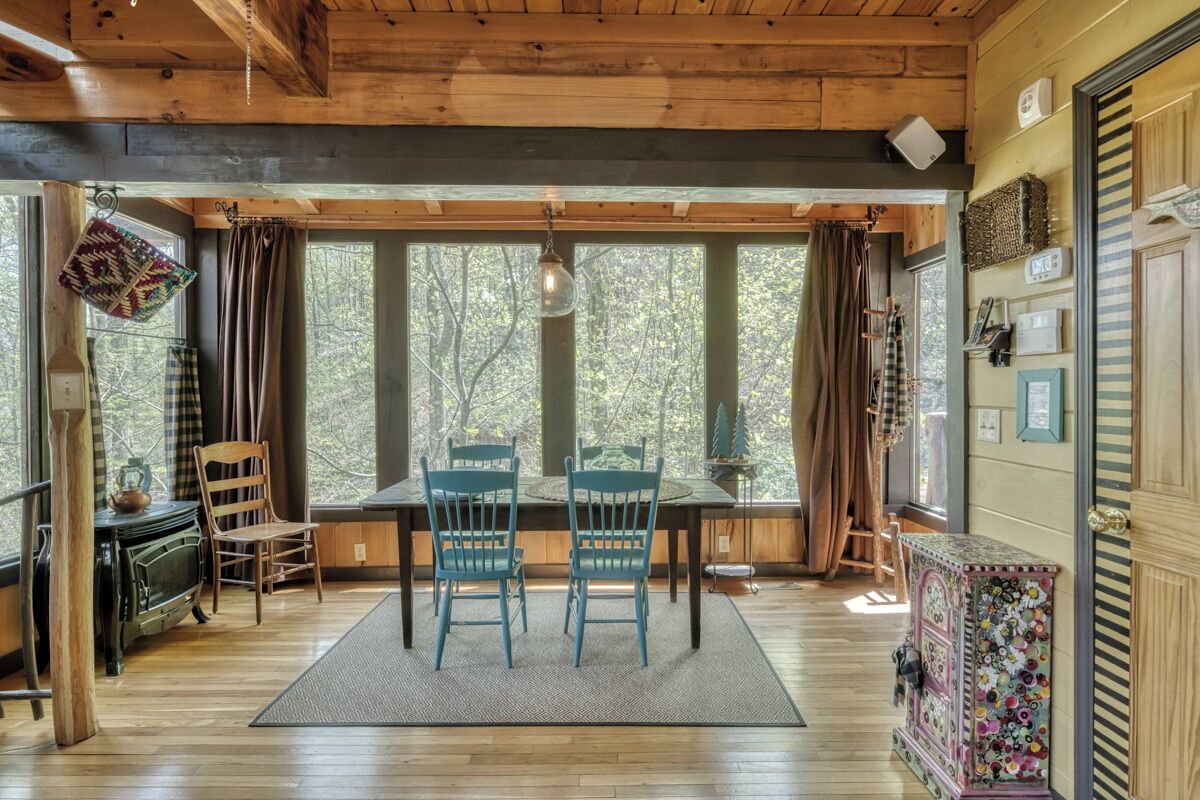 Ein gemütliches Blockhaus-Interieur mit einem Holzespeisetisch, zwei blauen Stühlen, einem Kamin und großen Fenstern mit Blick auf den Wald.