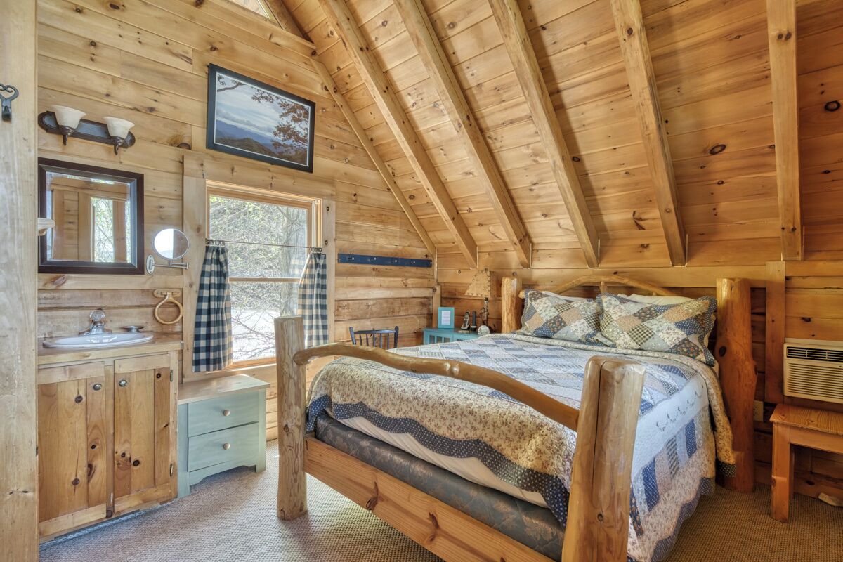 A wooden cabin bedroom with a bed, a dresser, a vanity, and a window.