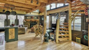 A rustic cabin interior with a wooden ceiling, a fireplace, a stone wall, a wooden staircase, and a dining area with a table and chairs. - Dancing Dragonfly (Sevierville)