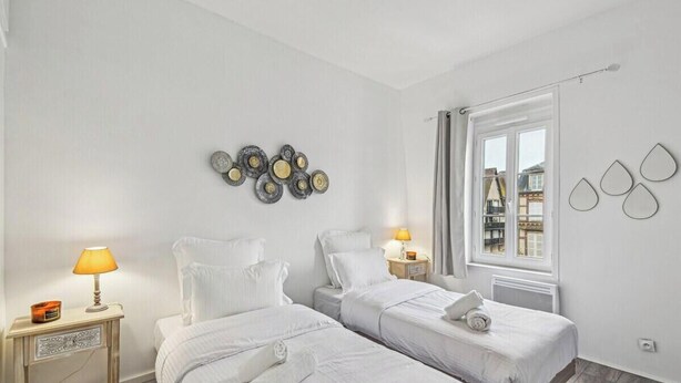 Habitación de hotel con dos camas, una ventana con cortinas, un adorno en la pared y una mesita de noche con lámpara.