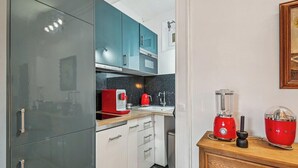 Una cocina compacta con armarios verde azulado, una cafetera roja, una licuadora y una encimera de madera.