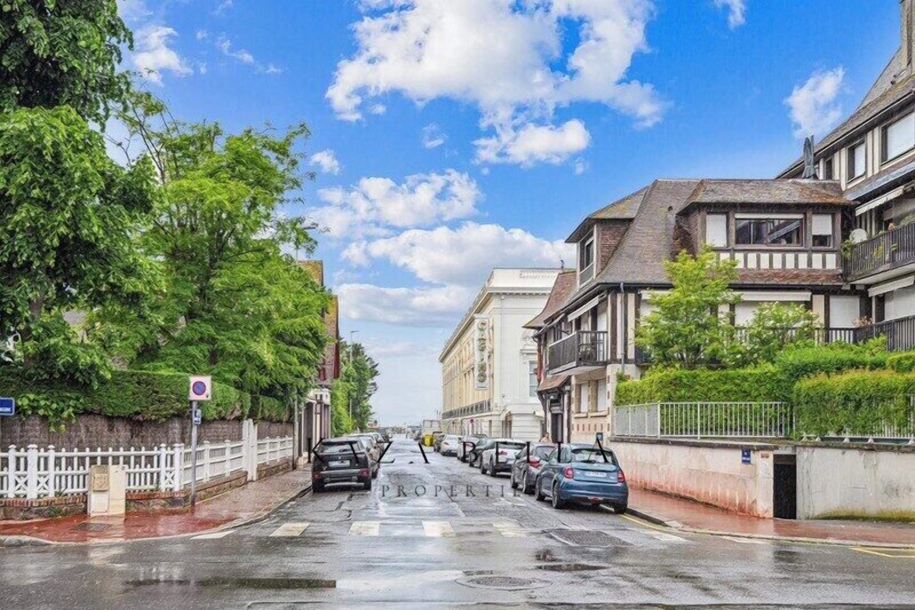 Straßenansicht mit parkenden Autos, einem weißen Zaun und Gebäuden mit Balkonen.