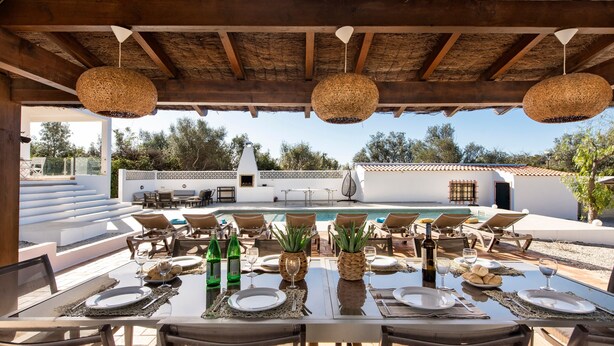 Ein Essbereich im Freien mit Blick auf einen Pool, einer Holzw pergola und weißen Wänden.