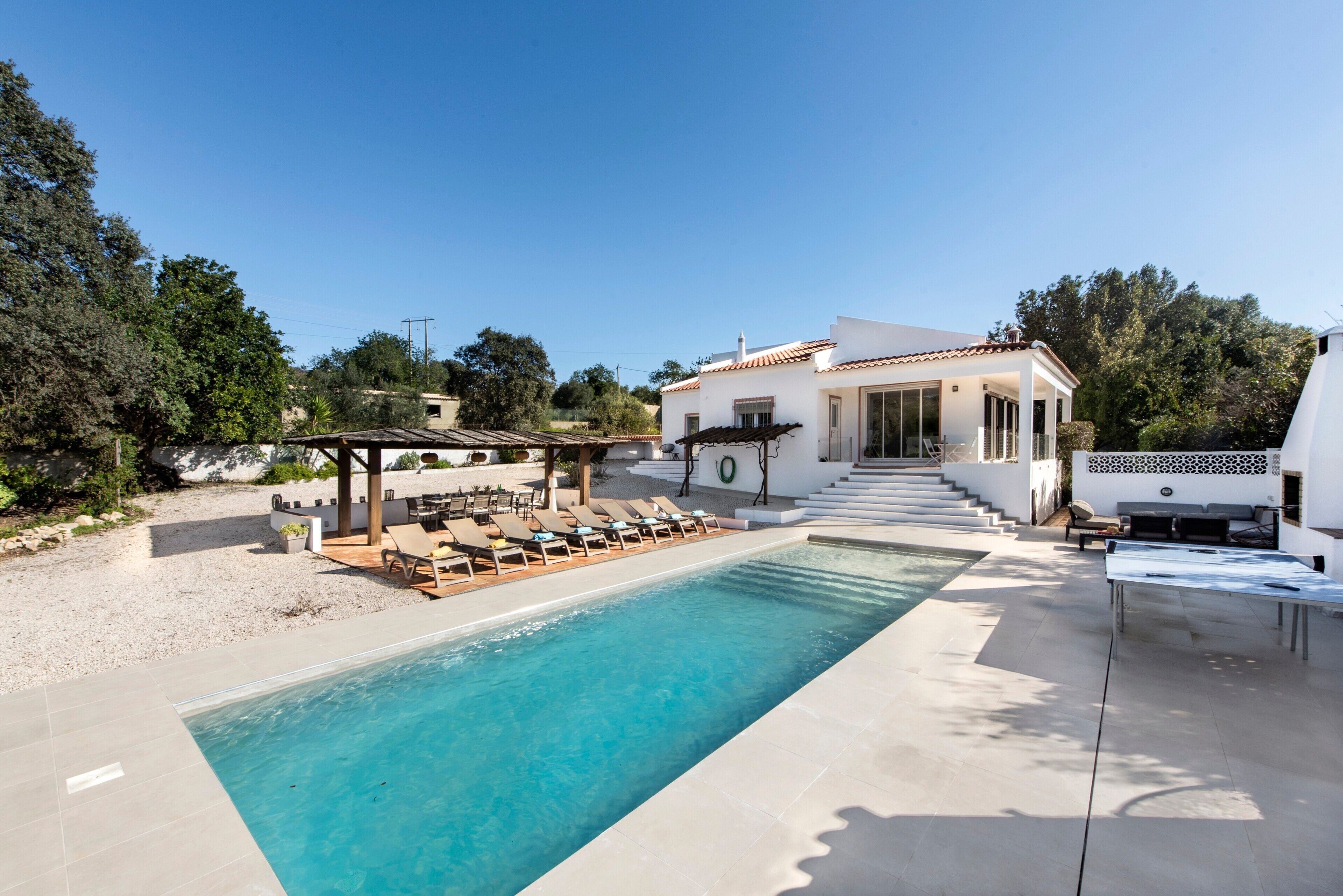 Une piscine avec des chaises longues, un espace de détente couvert et un bâtiment doté d’un toit en tuiles.