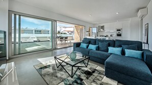 A modern living room with a sofa, a glass coffee table, and a view through large sliding glass doors to an outdoor balcony. - Modern Apartment with Shared Pool, Wi-Fi & Air Conditioning in Albufeira (Albufeira)