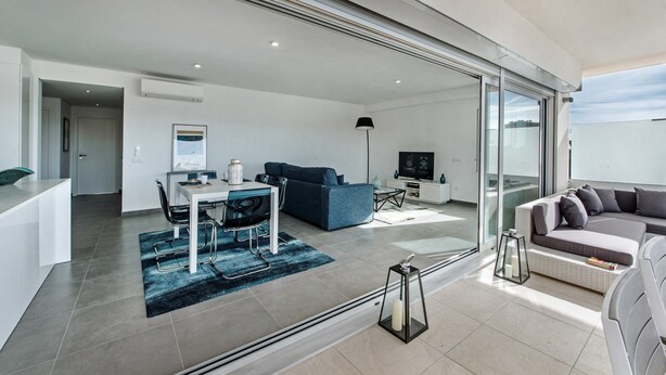 A modern living room with a dining area, a sofa, a TV, and a balcony. - Modern Apartment with Shared Pool, Wi-Fi & Air Conditioning in Albufeira (Albufeira)
