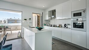 A modern kitchen with white cabinetry, a central island, and built-in appliances. - Modern Apartment with Shared Pool, Wi-Fi & Air Conditioning in Albufeira (Albufeira)