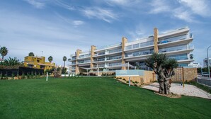 A multi-story hotel with balconies, a grassy lawn, and a tree. - Modern Apartment with Shared Pool, Wi-Fi & Air Conditioning in Albufeira (Albufeira)