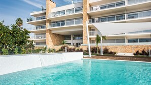 A modern hotel with a swimming pool, multiple balconies, and a stone facade. - Modern Apartment with Shared Pool, Wi-Fi & Air Conditioning in Albufeira (Albufeira)