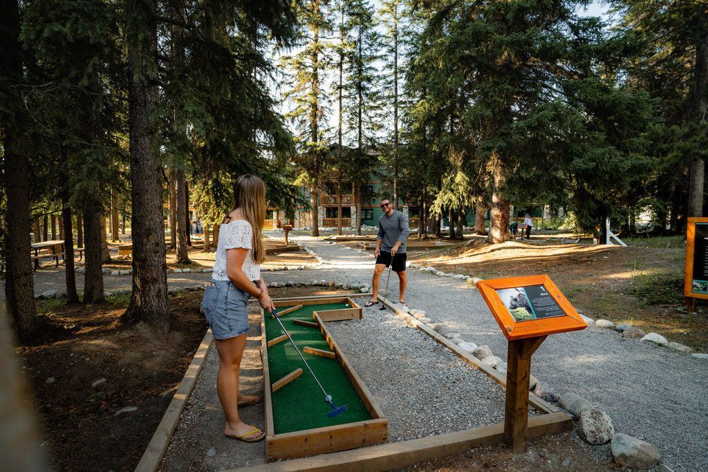 A croquet field with players, surrounded by trees and a wooden structure.