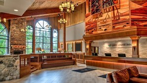 Eine geräumige Lobby mit Kamin aus Stein, einer Holztreppe und einem Empfangstresen im Lake Louise Inn.