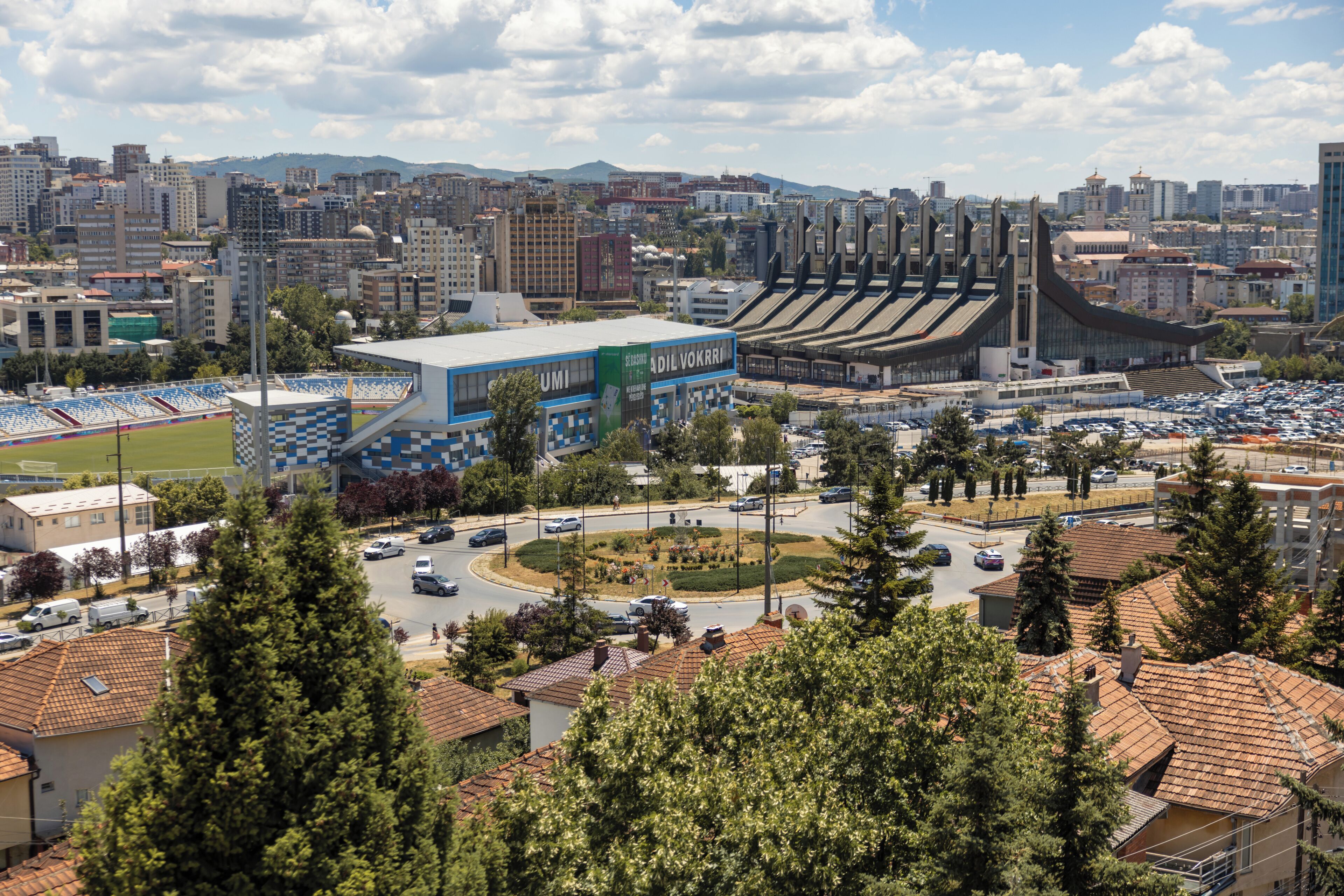 A stadium with multiple seating tiers, a parking area, and surrounding urban buildings.