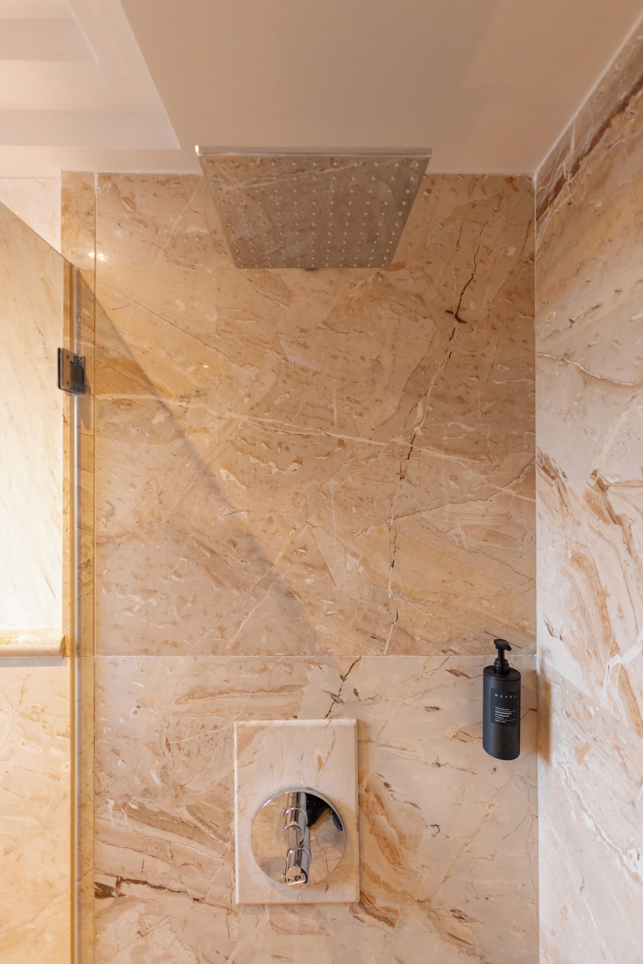 A bathroom with a marble wall, a showerhead, and a soap dispenser.
