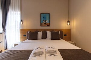 Habitación de hotel con cama, almohadas, un cuadro, dos lámparas de pared y una toalla doblada sobre la cama.
