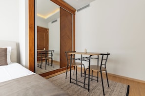 A bedroom with a bed, a desk with chairs, a mirror, and a patterned rug. - PRI ApartHotel (Pristina)