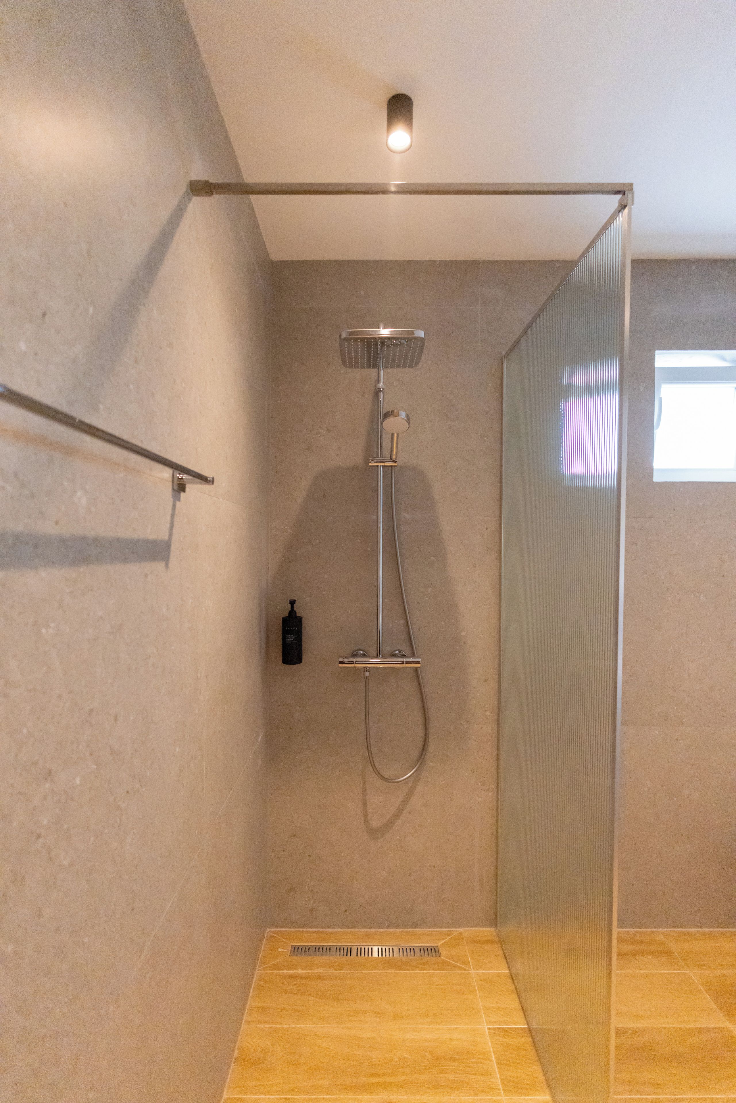 A modern shower with a glass enclosure, a handheld showerhead, and a wall-mounted control panel.