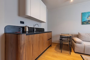A compact kitchenette with a built-in stove, a sink, and a small dining table. - PRI ApartHotel (Pristina)