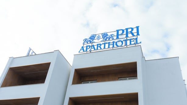 Un edificio moderno con un cartello che riporta "PRI APARTHOTEL" e balconi con dettagli in legno.