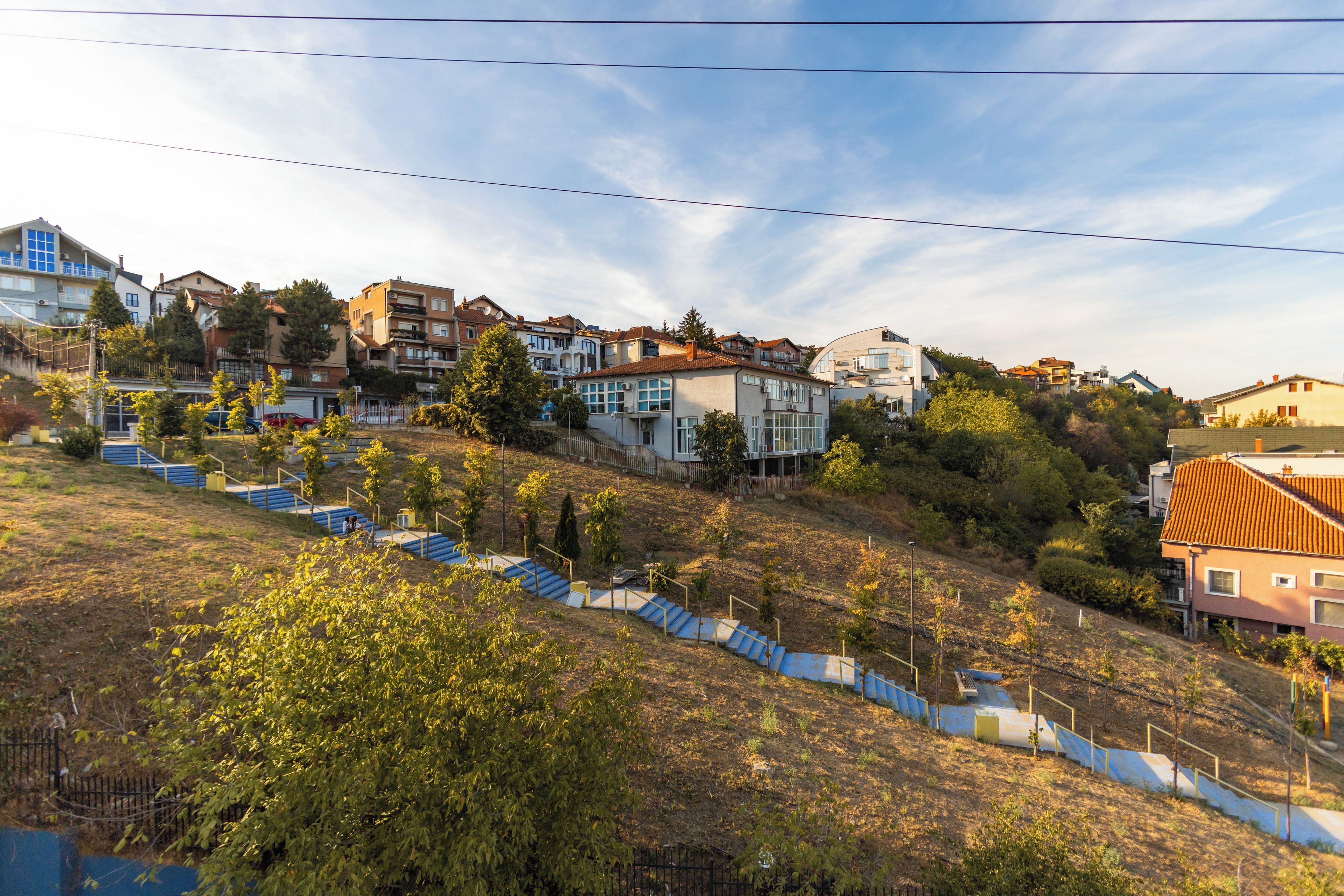 A residential area with multiple two-story houses, a staircase leading up a hill, and a clear sky.