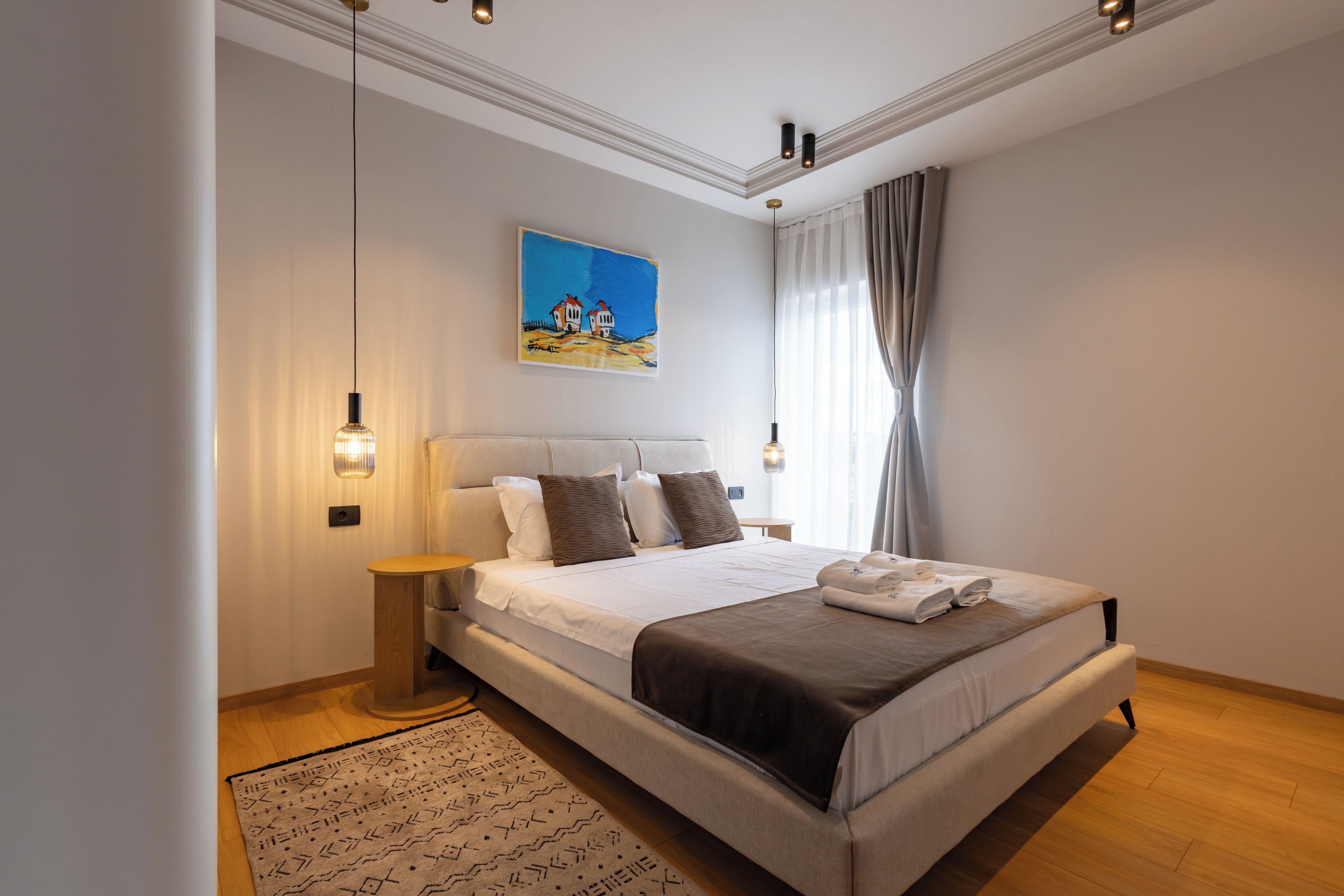Una camera da letto moderna con un letto grande, comodini, un quadro e vista sull'esterno.