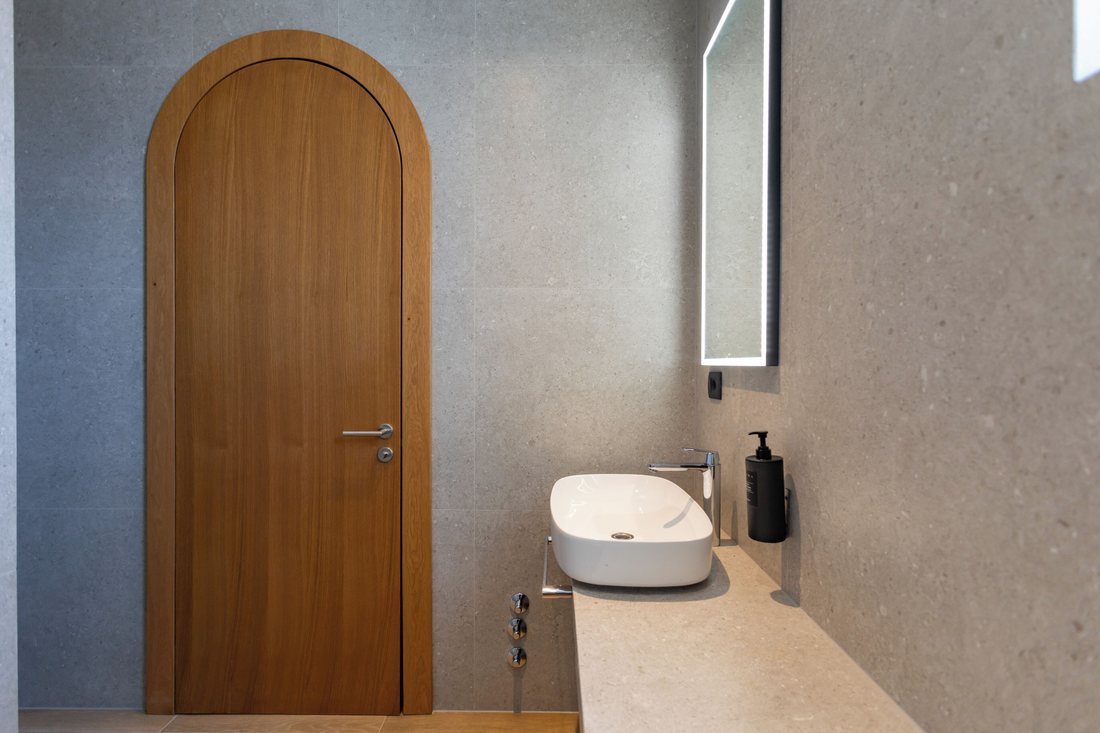 A bathroom with a wooden door, a white sink, and a mirror.