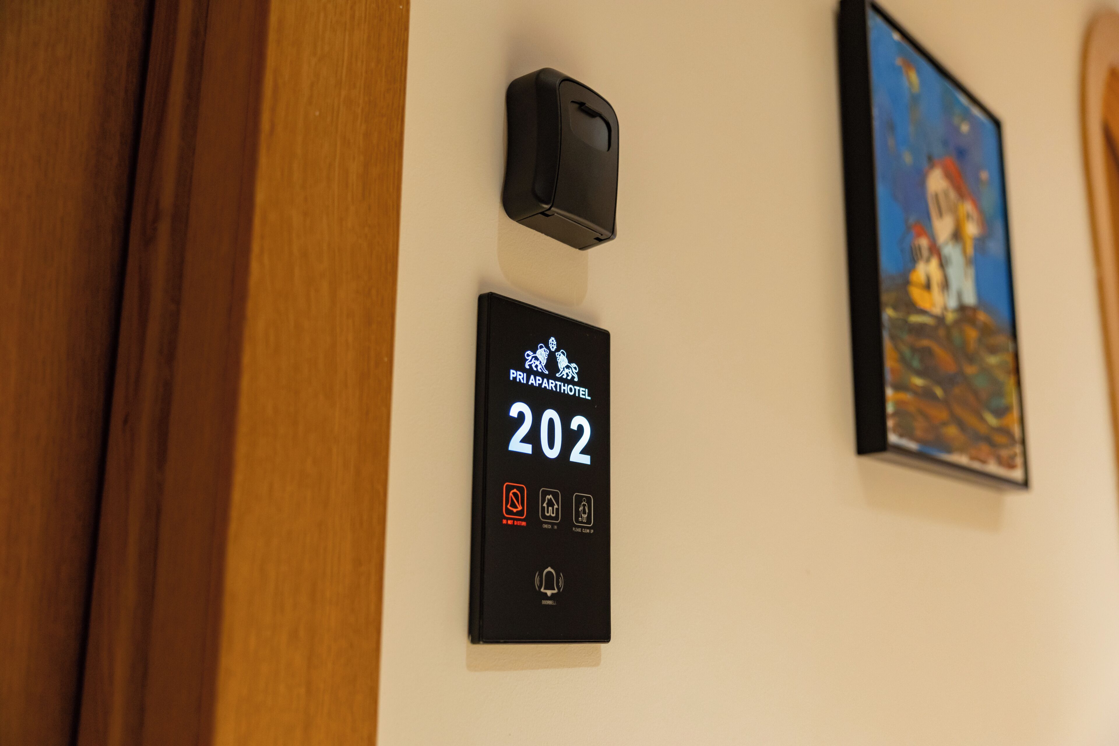 Habitación de hotel número 202 con un panel digital, un timbre y un cuadro en la pared.