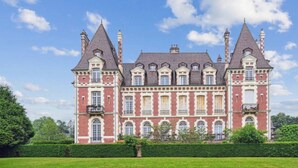 Een groot, historisch gebouw met meerdere torens en een symmetrische gevel, omgeven door goed onderhouden tuinen.