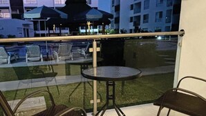 Un balcón con barandilla de vidrio, una mesa redonda y dos sillas.