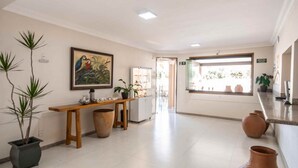 A hotel lobby with a wooden bench, potted plants, a painting, and a view through a window. - Pousada das Araras (Araçuaí)
