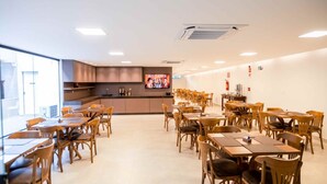 A spacious dining area with wooden tables and chairs, a kitchen in the background, and a large poster on the wall. - Pousada das Araras (Araçuaí)