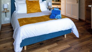 Quarto com teto de madeira, cama com roupa de cama branca e azul, cabeceira azul e piso de madeira.